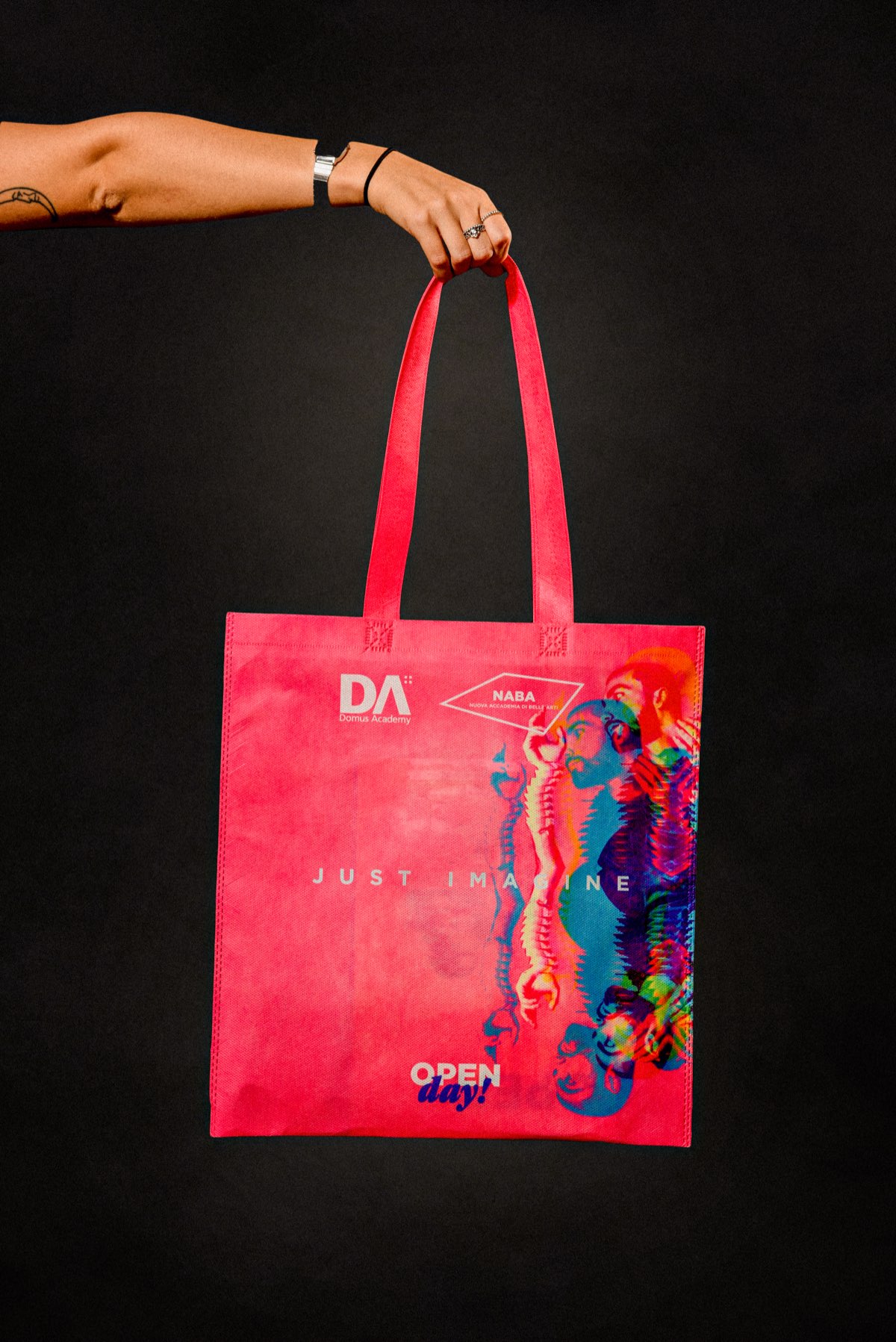 La tote bag rosa, tenuta per i manici, con la scritta JUST IMAGINE
