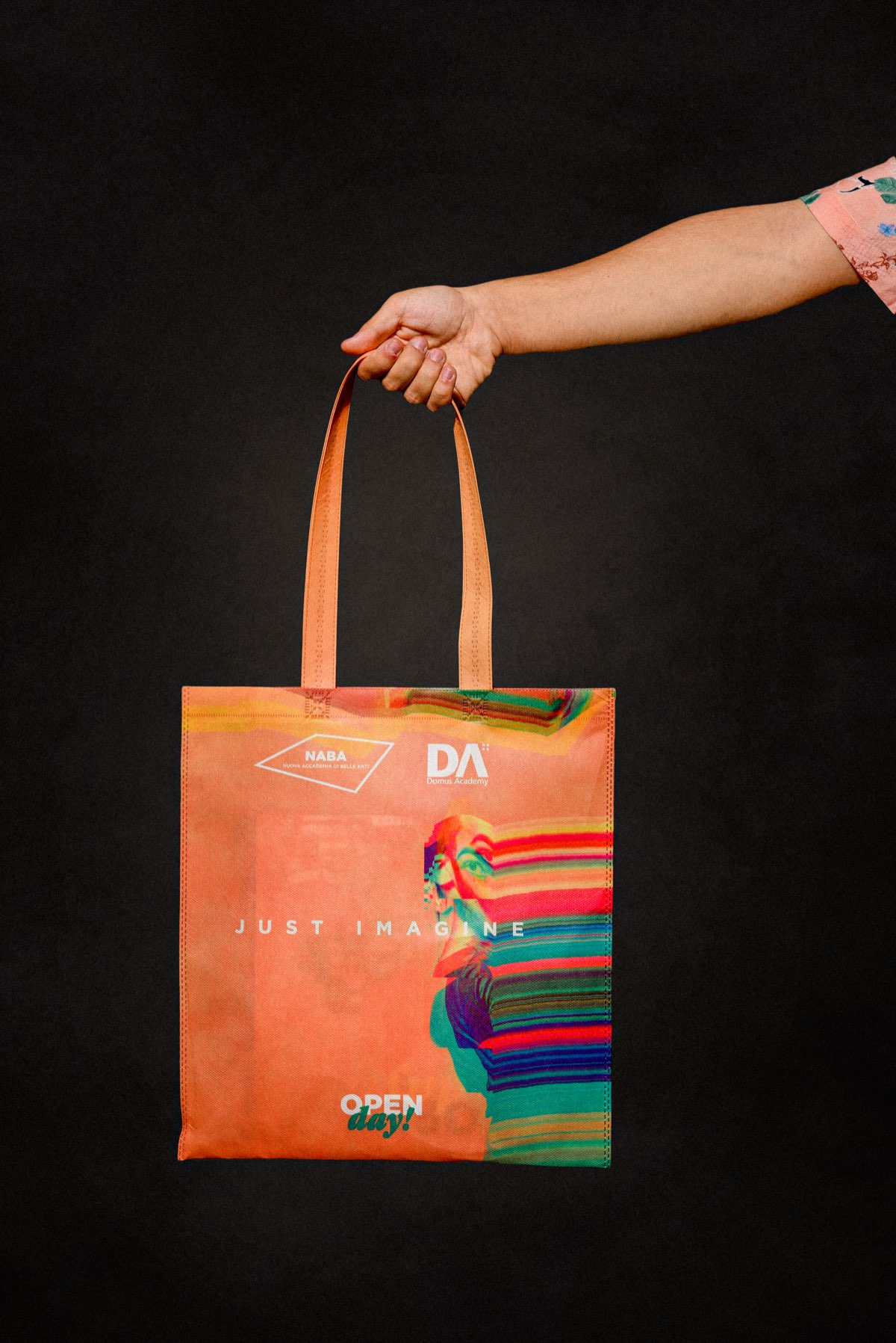La tote bag arancio, tenuta per i manici, con la scritta JUST IMAGINE
