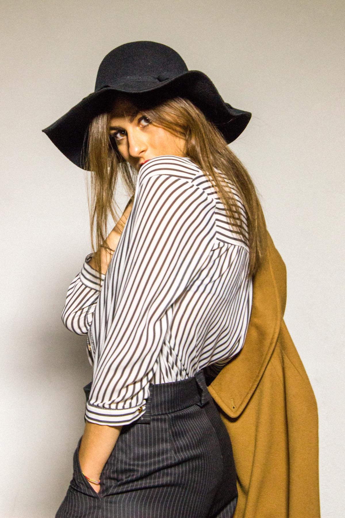 Di spalle, lo sguardo che torna verso l&rsquo;obiettivo, il cappotto cammello sulle spalle
