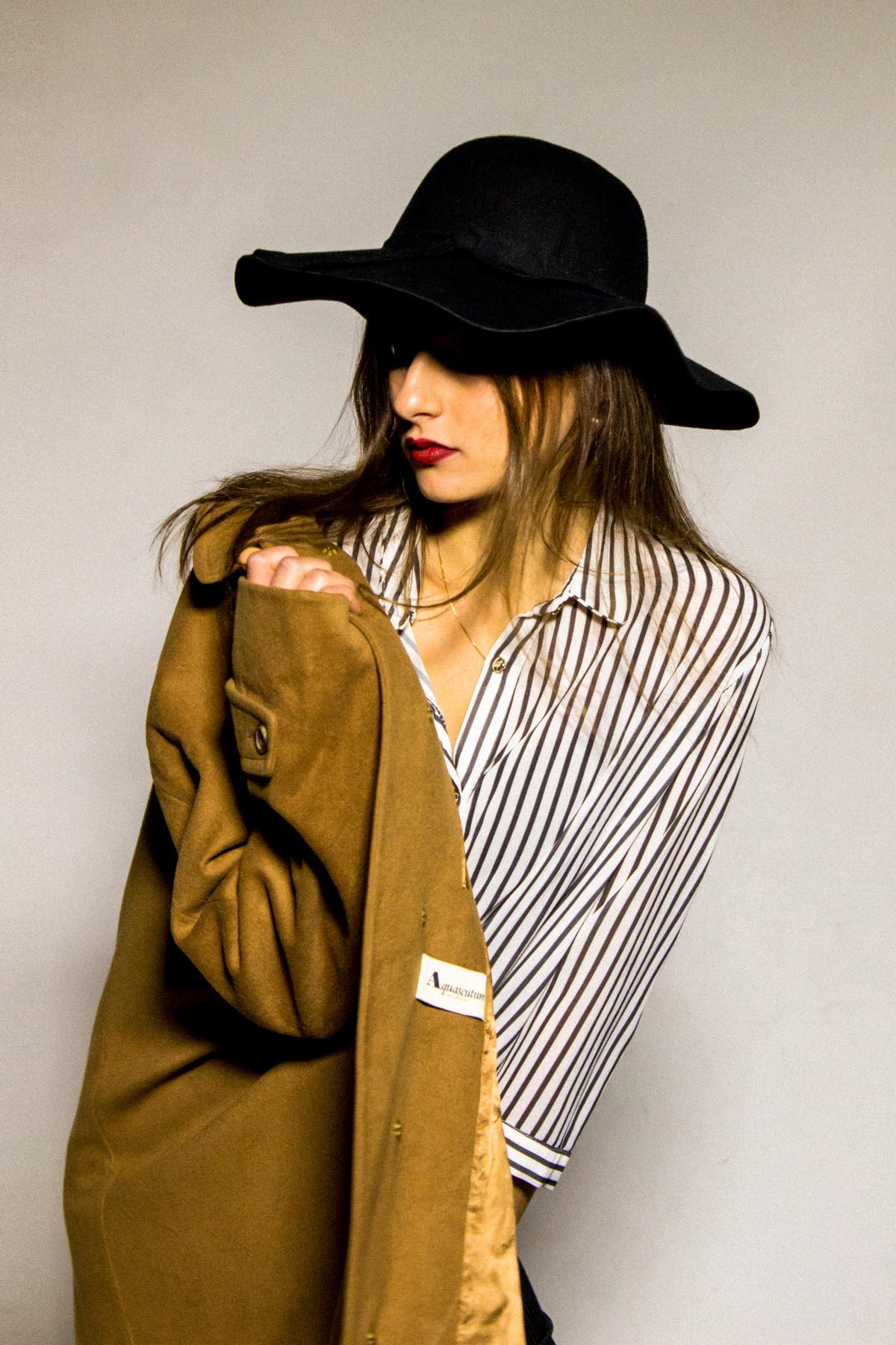 Lo sguardo basso, il cappotto aperto sulla camicia a righe