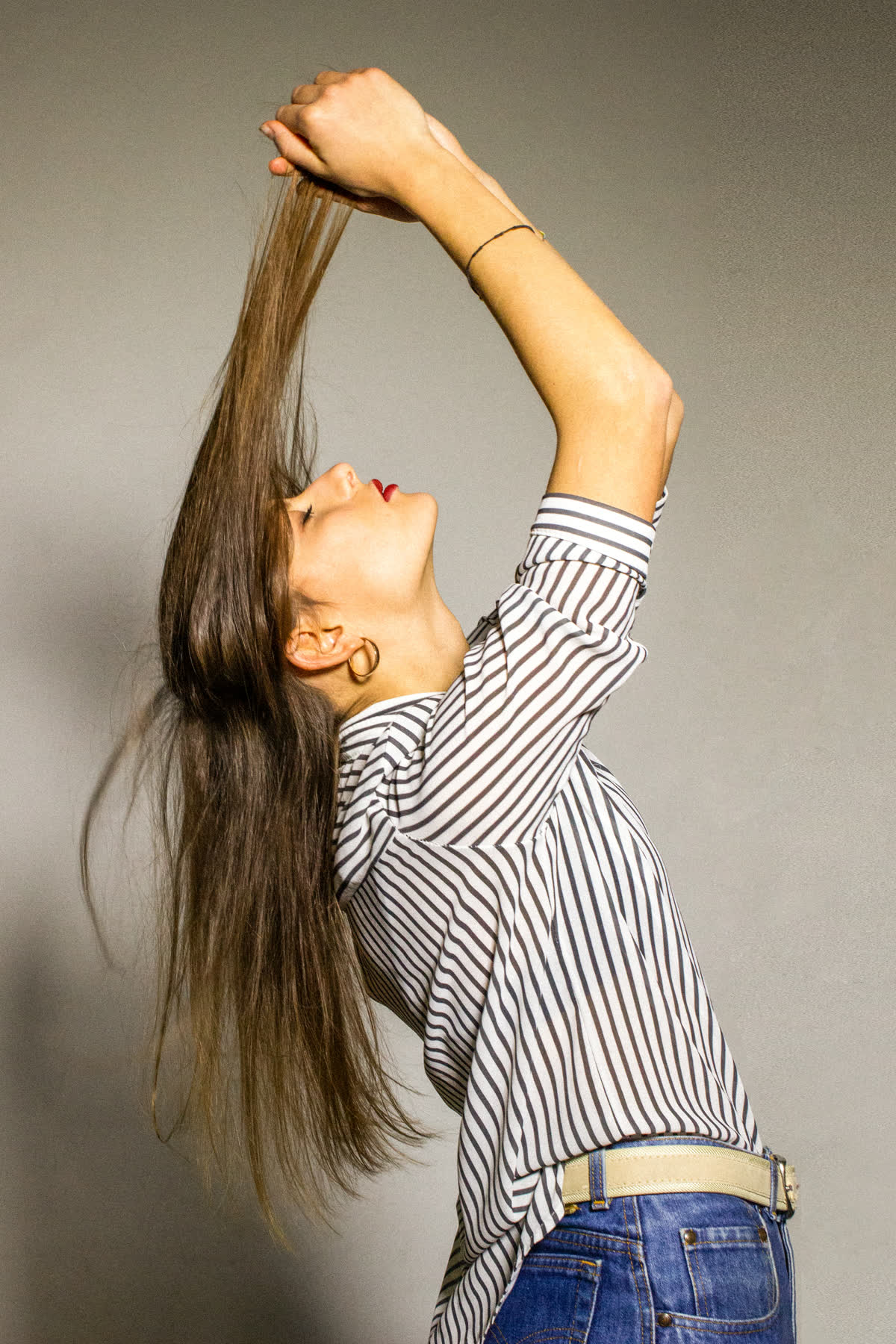 I capelli riuniti in una ciocca e tirati dritti verso l&rsquo;alto, il viso rivolto in su, la camicia a righe