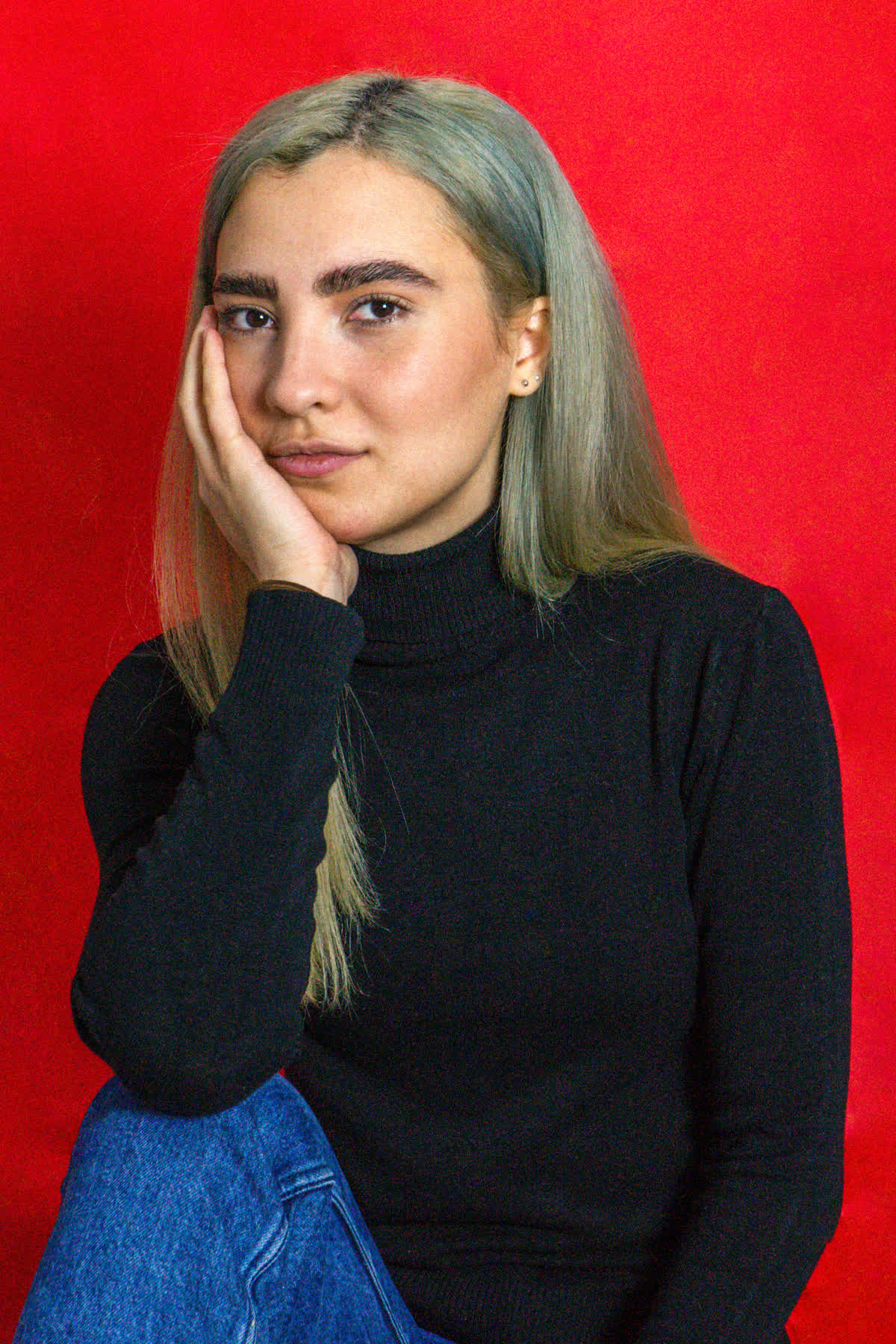 Su fondo rosso pieno, la mano vicino alla bocca, il sorriso trattenuto