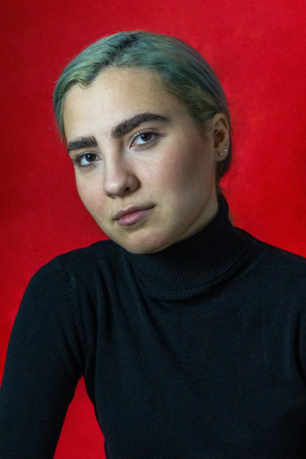 Su fondo rosso pieno, lo sguardo dritto in camera